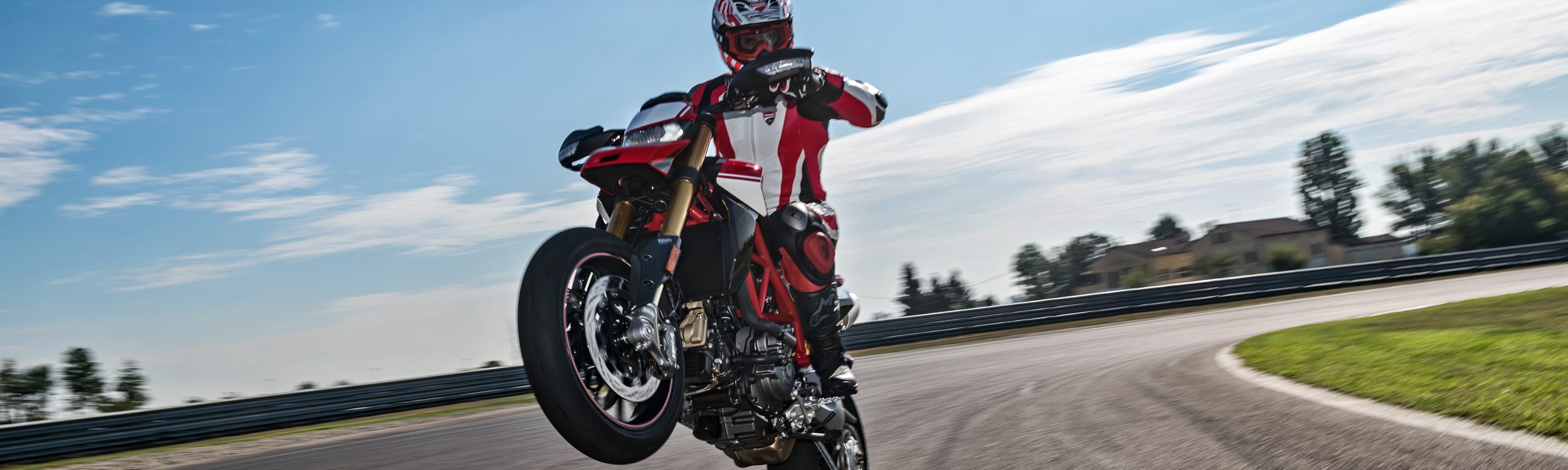 Motorcycle rider on a Ducati motorcycle doing a wheelie on a track.