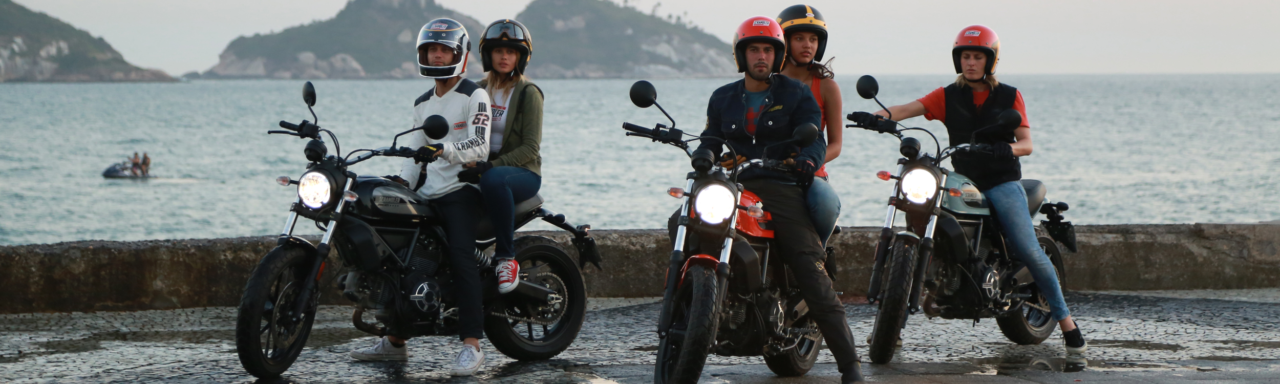 Group of motorcycle riders parked with ocean and cliffs in background.